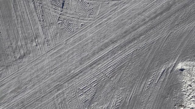 Snow-covered road intersection with tire tracks and shadows from streetlights, showcasing the gradual transition of snow texture and patterns in a winter landscape