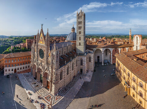 Aerial view of the Siena Cathedral, a symphony of striped marble and sculpted facade, rises majestically above the Piazza del Duomo, Siena, Italy.