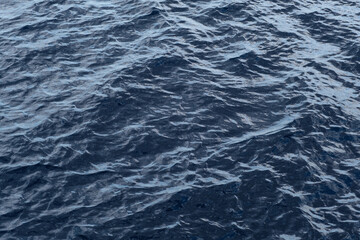 Dark blue ocean water surface with gentle waves reflecting light, creating a textured appearance in a serene aquatic environment