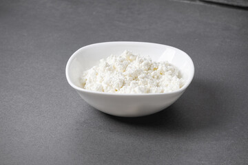 Cottage cheese in a white bowl on a gray surface in a kitchen setting showing fresh dairy food ready to serve.