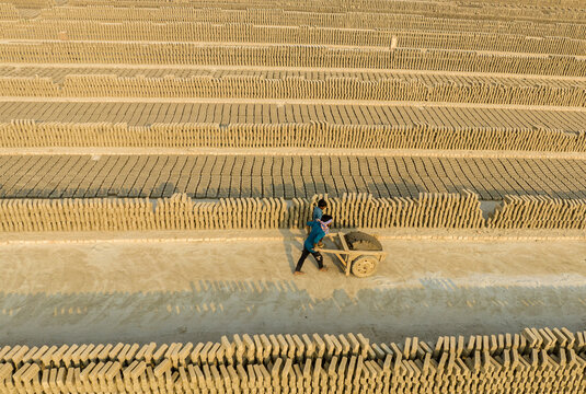 Aerial view of a worker pushing a cart through rows of drying bricks under the sun, Aminbazar, Dhaka Division, Bangladesh.