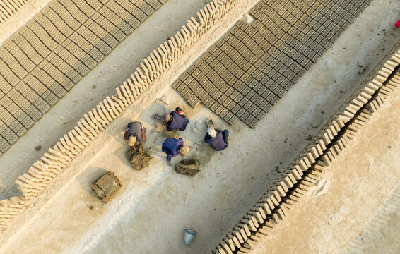 Aerial view of workers toiling amidst neatly stacked rows of bricks under the sun, creating a geometric pattern of textures and shadows, Aminbazar, Dhaka Division, Bangladesh.