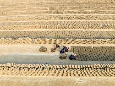 Aerial view of workers laying out rows of freshly made bricks under the warm sun, creating a textured landscape of earthy tones, Aminbazar, Dhaka Division, Bangladesh.