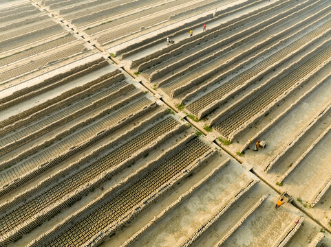 Aerial view of long rows of drying mud bricks stretch across the landscape under the sun, creating a textured pattern, Aminbazar, Dhaka Division, Bangladesh.