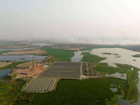 Aerial view of brick factory amidst waterlogged fields, juxtaposing industrial activity with the natural landscape, Aminbazar, Dhaka Division, Bangladesh.