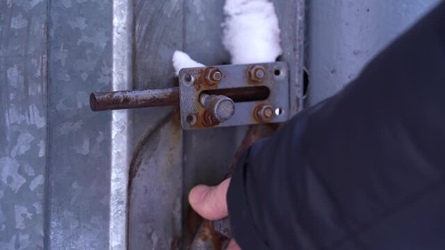 A man's hand tugs on the handle of the iron gate door, tearing it away from the fence