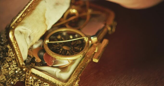 Close up of hand opening small gold case containing emerald brooch and vintage jewellery pieces. Suitable for heritage, fashion, documentary use.