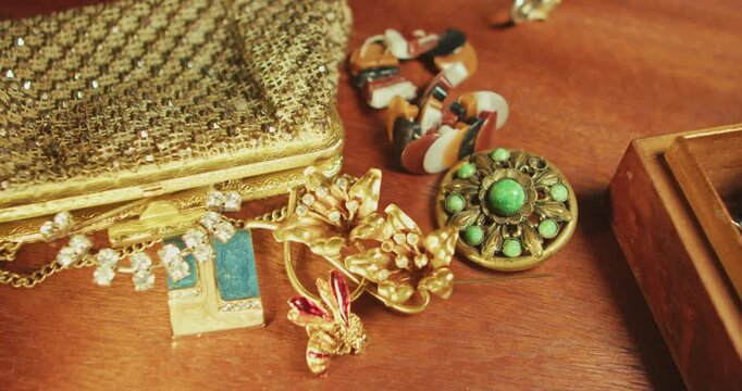 Slow pan across vintage jewellery, brooches and fashion accessories arranged on wooden table surface. Suitable for heritage, lifestyle, documentary use.