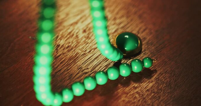 Close up of green beaded necklace being laid on wooden table with vintage jewellery and small trinkets. Suitable for heritage, fashion, documentary use.