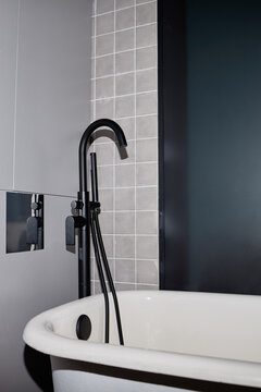 Modern freestanding bathtub with black faucet and handheld showerhead positioned against tiled wall in contemporary bathroom interior, showing clean minimalist design elements