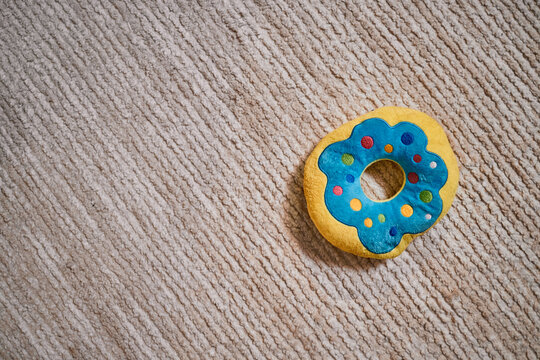 Colorful plush toy donut lying on textured carpet, vibrant blue and yellow design with multicolored dots, soft surface suggesting use as pet toy or child plaything, ample copy space