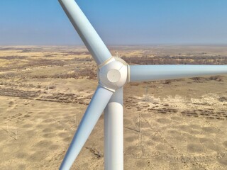 aerial view - A close-up view of the center hub and blades of a white wind turbine, overlooking an arid, desert-like landscape below © PakLam