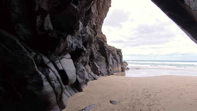 Blick aus der dunklen Felsenh&ouml;hle auf den einsamen Sandstrand und Meer: Dramatischer Lichtkontrast, K&uuml;stenidylle und Naturabenteuer, verborgene Sch&ouml;nheit, Expedition, Landschaft, K&uuml;ste
