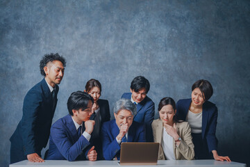 ノートパソコンの前に集合する様々な世代のスーツを着た男女