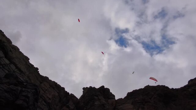Paragliders flying high above rocky mountain landscape, hang gliding, paragliding, rock formations, tandem flight, sport, freedom, extreme sport, lift, wind, clouds, sky, adventure, active vacation