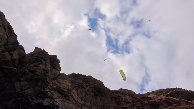Paragliders flying high above rocky mountain landscape, hang gliding, paragliding, rock formations, tandem flight, sport, freedom, extreme sport, lift, wind, clouds, sky, adventure, active vacation
