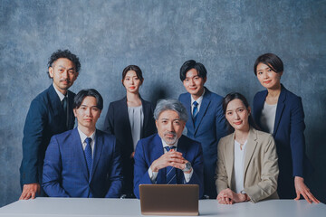 ノートパソコンの前に集合する様々な世代のスーツを着た男女