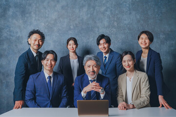 ノートパソコンの前に集合する様々な世代のスーツを着た男女