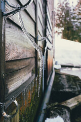 木造建築の板壁と針金を伝い伸びるいびつな形の氷柱 / Distorted icicles growing along wire on wooden building wall