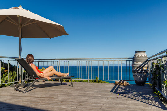Woman sunbathing on veranda with ocean view