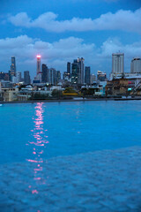 Fototapeta premium Skyline of Bangkok at dusk. The cityscape features numerous skyscrapers of varying heights, including prominent slender towers and denser office buildings, all silhouette against a deep blue sky.