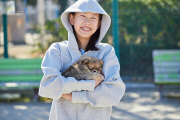 春の晴天の公園で可愛いポメラニアンの子犬と遊んでいる十代の女の子の姿