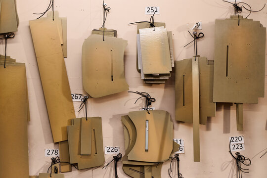 Leather pattern templates hanging on workshop wall, various shapes and sizes organized with numbered tags, essential for crafting leather goods and ensuring precise cutting process