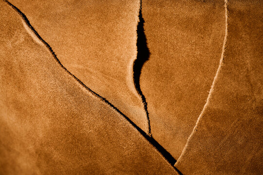 Closeup showing textured brown leather pieces overlapping in workshop setting, highlighting natural grain and raw edges, suitable for illustrating leathercraft or material quality