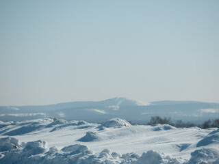 Winter landscape with snowdrifts and distant hills under a clear blue sky. Cold season scenery for nature background or greeting card. © Olesia Basova