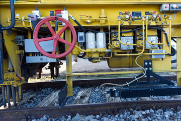 Fototapeta premium A complex assembly of industrial machinery featuring yellow steel frames, a red manual control wheel, and intricate hydraulic lines over railway tracks