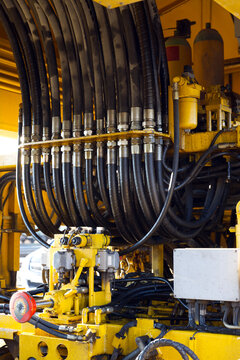 A detailed close-up of heavy-duty hydraulic hoses and yellow machinery components. The intricate network of black pressurized lines and industrial fittings 