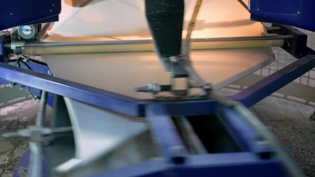 Fabric being processed inside an automated machine in a modern textile factory. Professional industrial footage reflecting mass production, technical control and textile manufacturing technology.