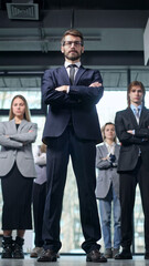 Fototapeta premium A man in a suit stands with his arms crossed in front of a group of people