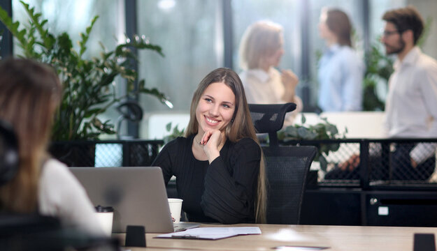 A woman is sitting at a desk with a laptop and smiling