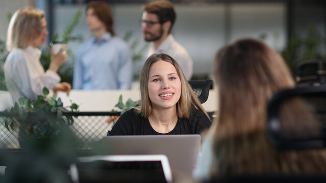 A woman is sitting at a desk with a laptop and smiling