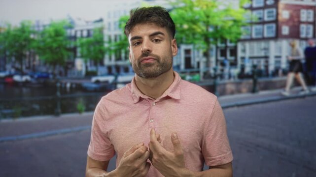 Young hispanic man wearing pink polo shirt counts fingers and glances aside on street; planning and concentration.