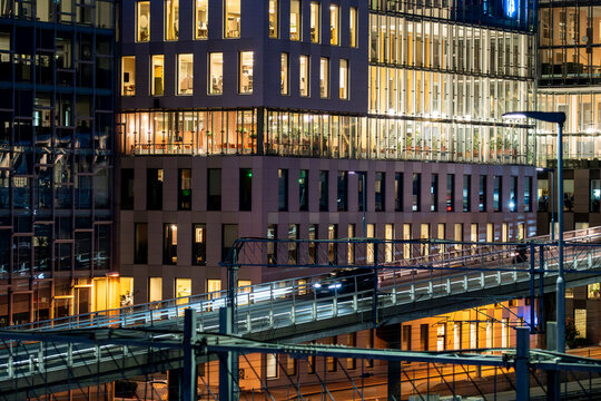 Glass bridge walkway linking office buildings with urban night lights and reflections in Oslo Barcode district
