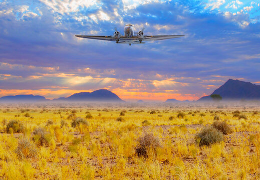 A twin-engine vintage propeller plane flies over the Namib Desert - Typical landscape of Namibia between Kalahari and Namib desert - Namibia