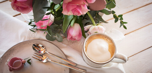 Flower decoration for a mother's day breakfast. Pink roses, tulips, and ranunculus arranged on a white table. Lifestyle background. Close-up from above.