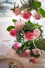 Flower decoration for a wedding table. Pink roses, tulips and ranunculus arranged on a tiered stand. Vertical lifestyle background for festive occasions.