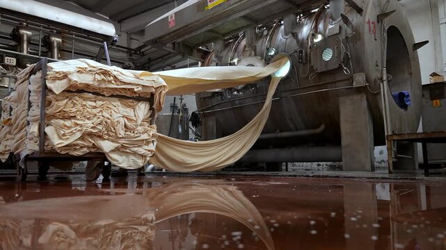 Flowing fabric emerging from large dyeing machines inside a textile factory. Professional industrial footage reflecting technical process, production discipline and large scale manufacturing.