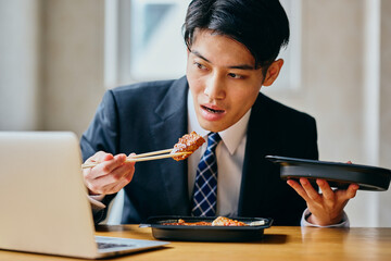 Asian businessman eating meal while working on laptop