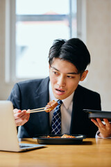 Asian businessman eating meal while working on laptop