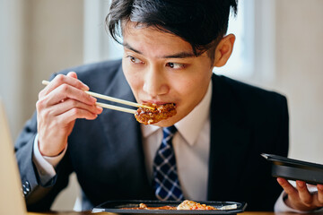Asian businessman eating meal while working on laptop