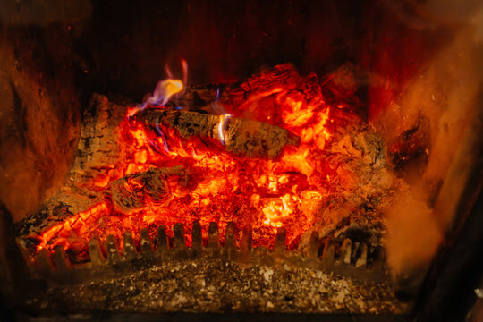 Glowing embers and flames inside a fireplace with charred wood logs and ash visible, creating a warm and inviting atmosphere in a cozy setting