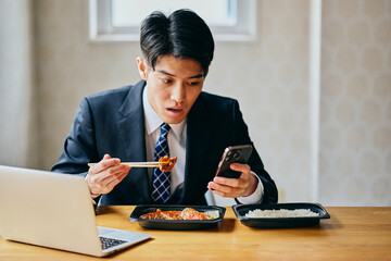 Asian businessman eating lunch while checking smartphone at desk
