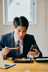 Asian businessman eating lunch while checking smartphone at desk