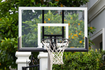 Outdoor basketball hoop in front of a green hedge and a house. © Rattanachat