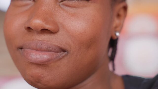 Closeup black woman smiling with hydrated lips, subtle gloss, ear stud, soft pink background, beauty blogger persona, natural skin texture, warm lighting, confident expression for skincare campaign