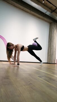 Fit young woman doing glute bridge kickbacks with a mini stability ball in a studio, focusing on toning and core strength. Vertical video